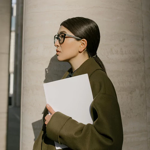 A woman wearing glasses and a green coat holds a white paper